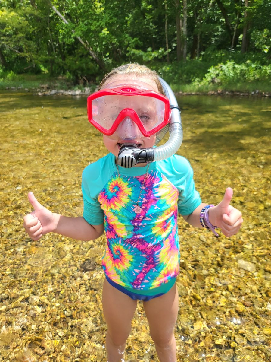 A kid giving a shaka sign while snorkeling in the clear water of Bull Creek